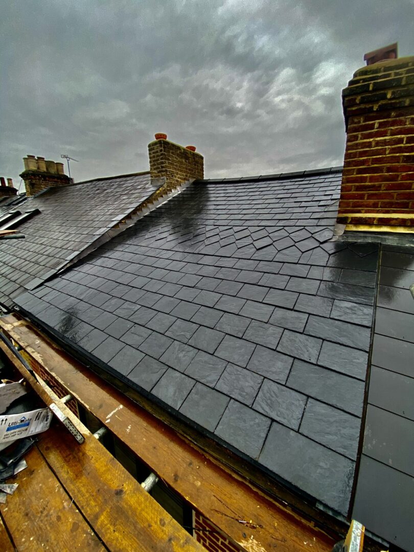 a slate roof with neatly arranged dark tiles, featuring two brick chimneys against an overcast sky