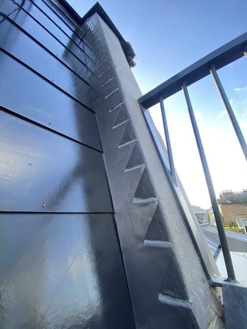 close-up view of a dark metallic staircase with triangular tread patterns. It is accompanied by a metal railing and set against a clear sky