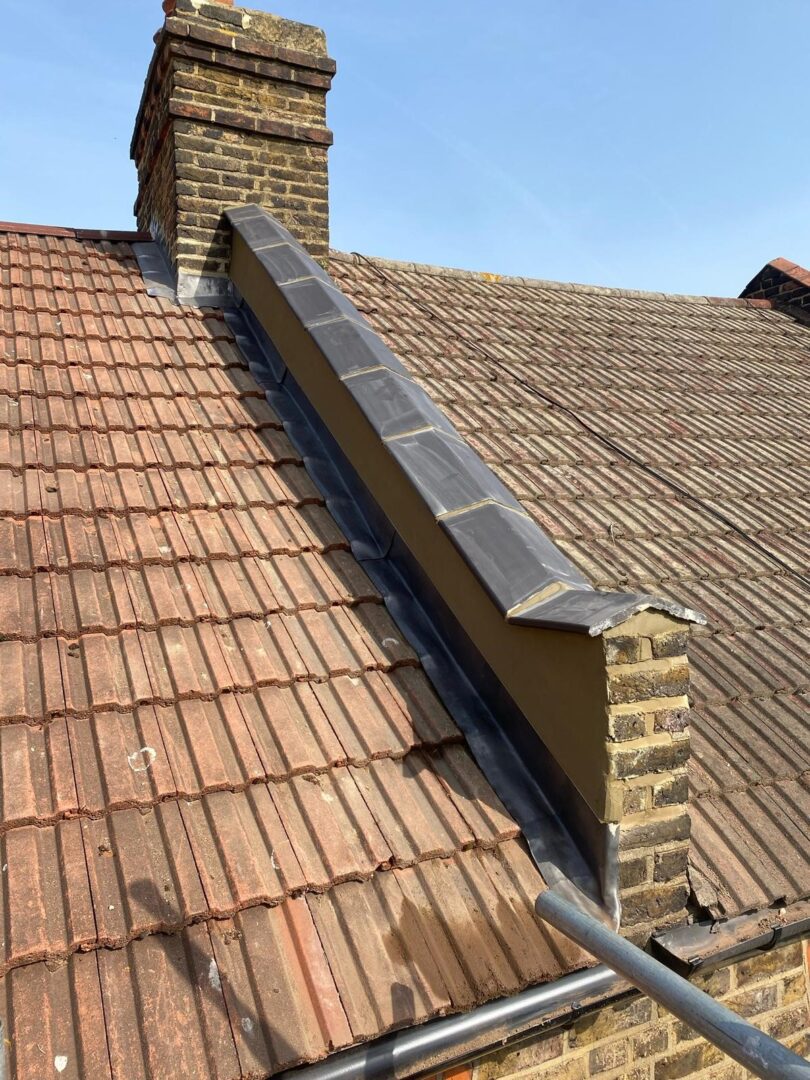 A sloped, brown-tiled roof with a brick chimney on the left and a grey gutter running along the bottom. The clear blue sky serves as the backdrop